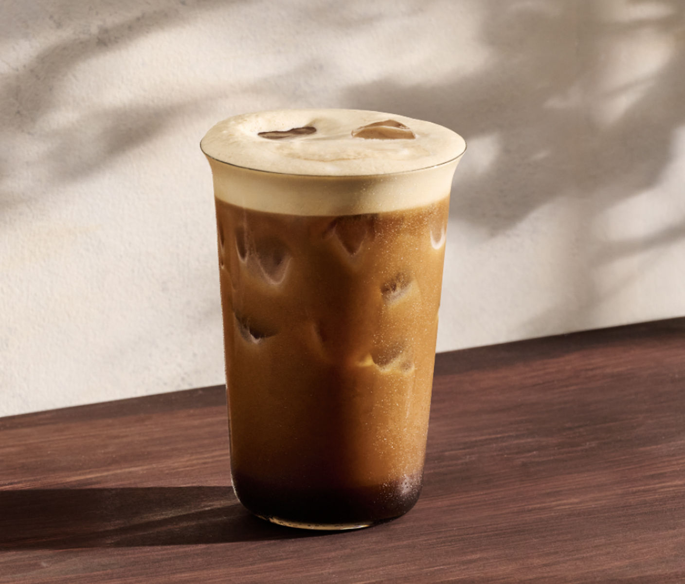 Un aerocano au caramel dans un grand verre, servi avec de la glace. Une mousse légère descend en vagues et se fond graduellement à l’espresso foncé au fond du verre.